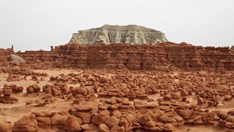 Gorgeous-stunning-tilt-up-shot-of-the-beautiful-Goblin-Valley-Utah-State-Park-mushroom-rock-formations-with-red-and-white-Butte's-in-the-background-on-a-warm-sunny-summer-day