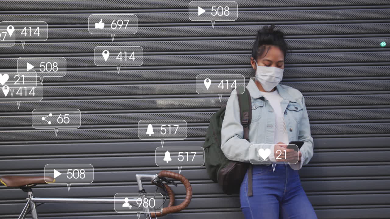 Animation of social media icons and numbers on banners over woman in face mask using smartphone