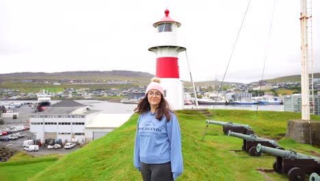 female tourist looks into camera in front of lighthouse at skansin in torshavn