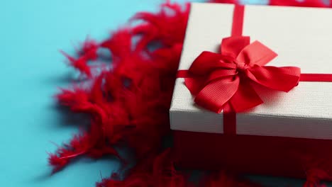 Box-with-a-gift--tied-with-a-ribbon-placed-on-red-feathers