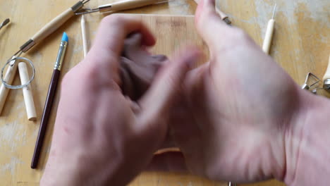 timelapse of an artist or sculptor using his hands and tools while sculpting a piece of brown modeling clay into a face mask on a wooden table in the art studio in fast motion