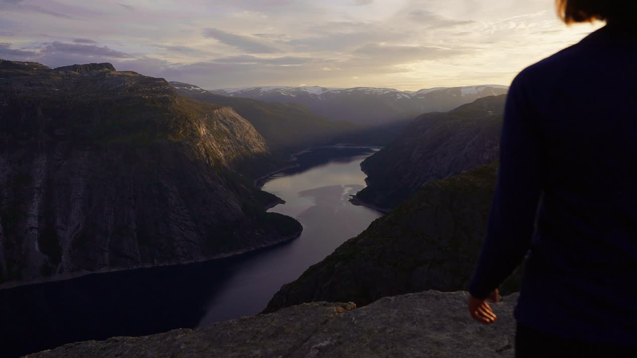 Woman standing on cliff at sunset, overlooking a fjord in Norway, feeling peaceful, Trolltunga