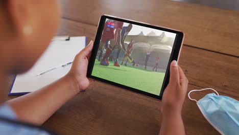 composite of woman sitting at table with face mask, watching hockey match on tablet