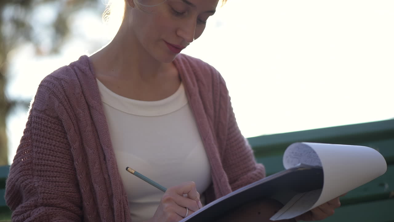 Woman writing on paper on a bench in the park on a sunny day
