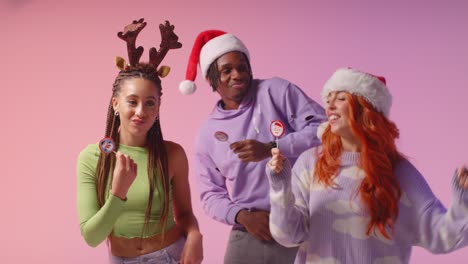 studio shot of gen z friends dancing at christmas party wearing santa hat and reindeer antlers 1