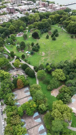 a drone tilt-up shot from senator street, capturing owl’s head park in brooklyn, gradually revealing the park's greenery and surrounding urban landscape.