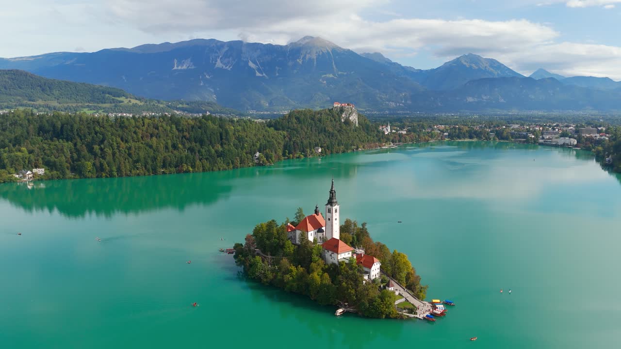 Drone orbits right around Lake Bled island and distant castle, Aerial