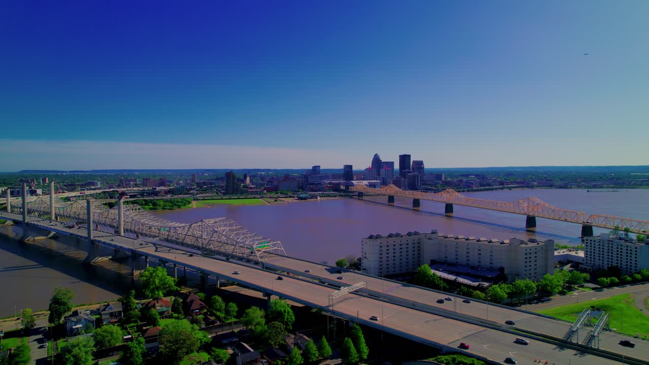 Stunning aerial footage showing traffic crossing Louisville's iconic bridges over the Ohio River, with clear views of the city skyline under vibrant skies.