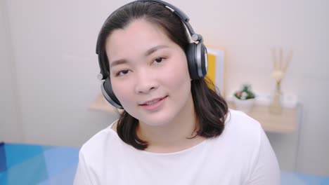 asian woman smiling using the bluetooth headphone for listening to music and looking at the camera so lovely lie in bed