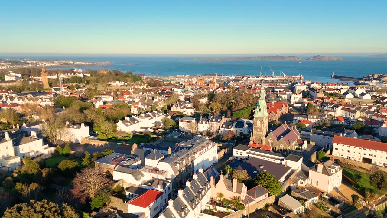 High circling drone footage of the roof tops of St Peter Port Guernsey in the golden hour with views across town and the harbour to Herm and Jethou