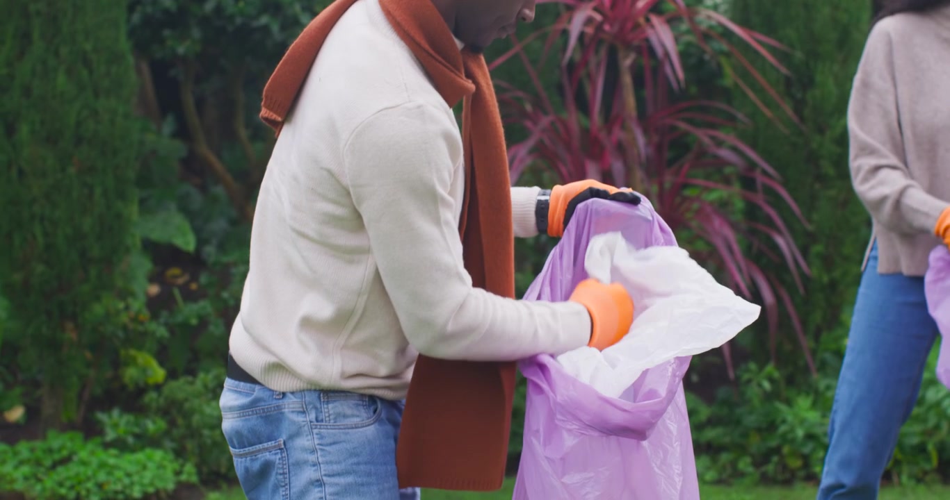 African American couple with orange gloves picking up paper into purple bags while cleaning lawn