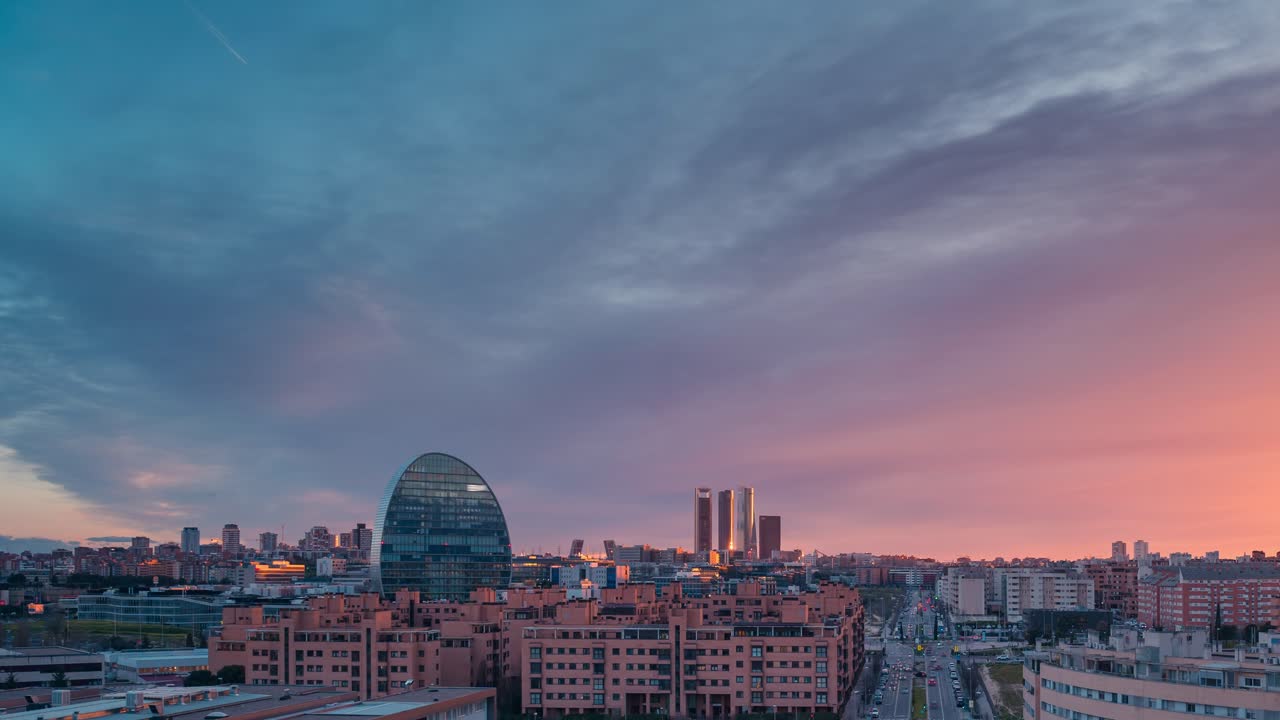 Timelapse dello skyline della moderna città europea di Madrid al tramonto, con luce dorata e nuvole rosse durante l'ora blu. Zoom in timelapse dal giorno alla notte che mostra la torre BBVA e i grattacieli dell'area direzionale delle 5 torri
