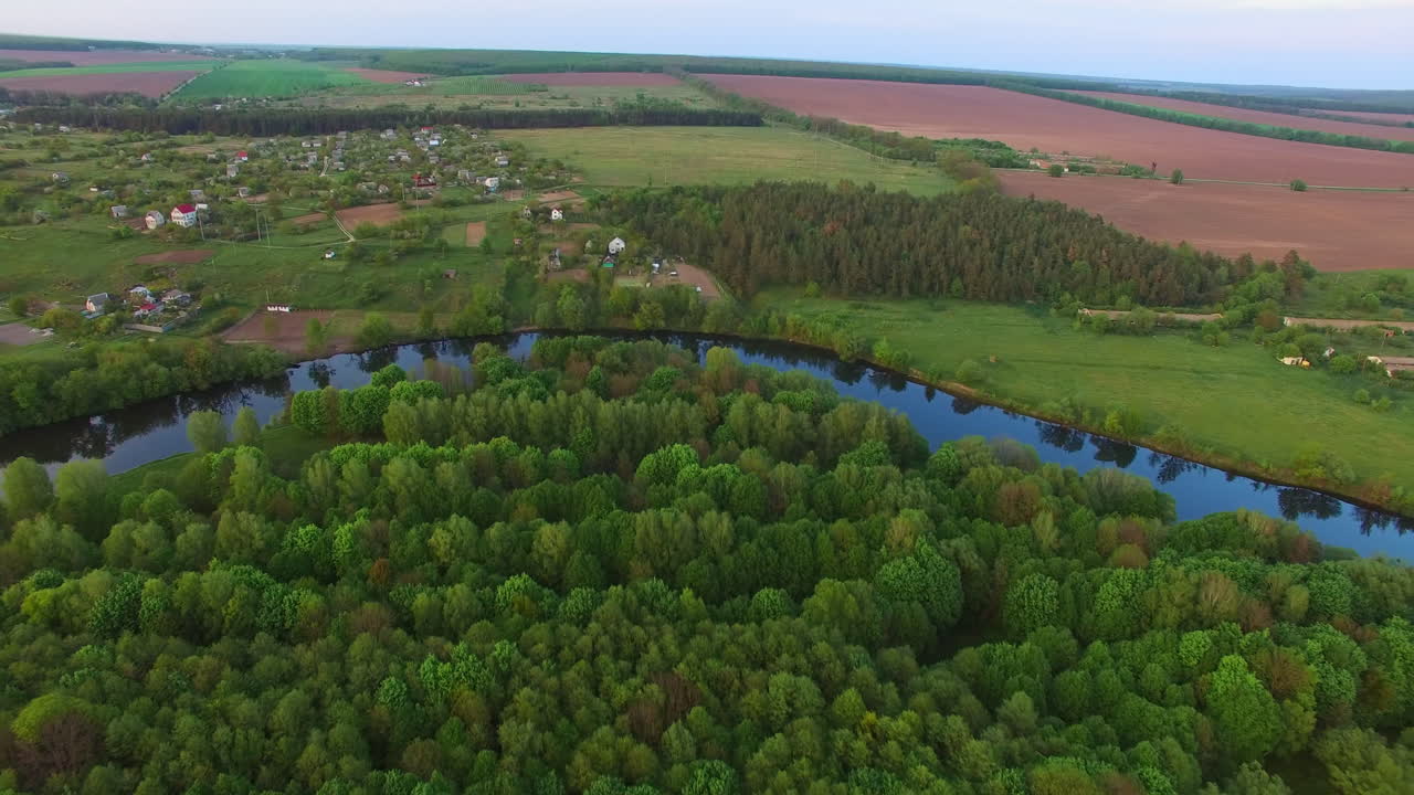 Green nature forest outlined with thin river. Rural territory nearby the woods and farmlands. Aerial view.