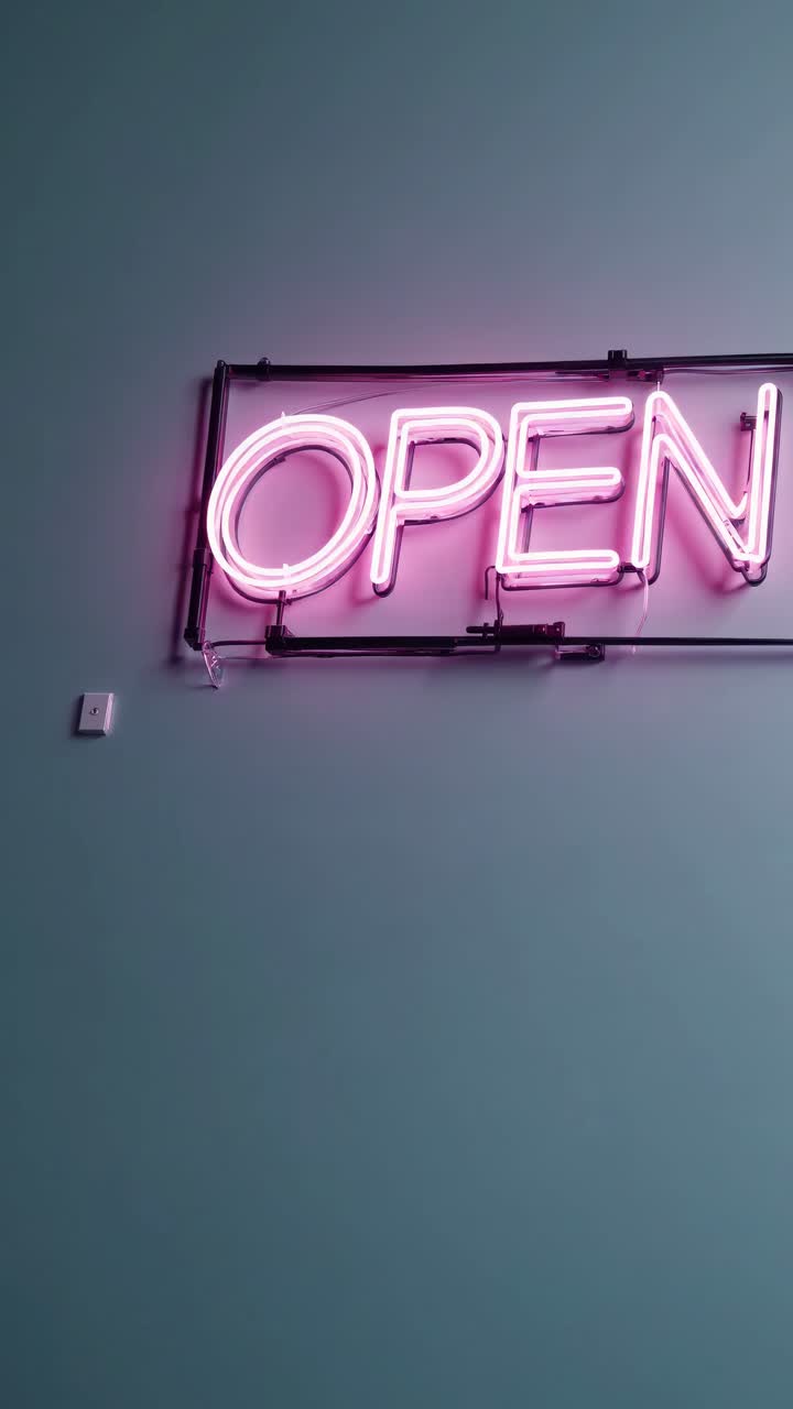 Neon 'OPEN' sign in pink against a teal wall, captured from a low angle