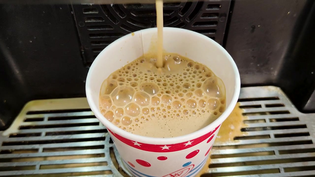 Primo piano di caffè caldo appena fatto erogato in un bicchiere di carta da un distributore automatico. Ideale per progetti in ambiente di lavoro, ospitalità, comodità e cultura del caffè
