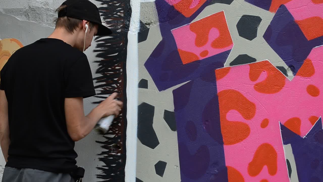 The artist draws graffiti on a fence, abstraction