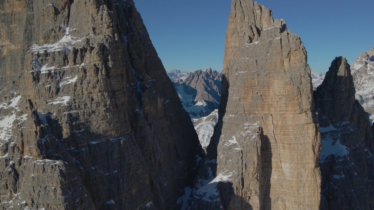 Aerial view flying between Tre Cime South Tyrol mountain rock formation reveal snowy scenic valley landscape