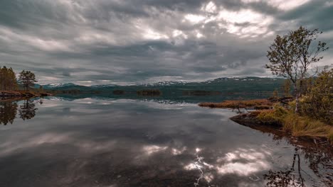 las nubes, coloreadas por el sol poniente en tonos de rosa, gris y amarillo, fluyen sobre las tranquilas aguas del lago como un espejo