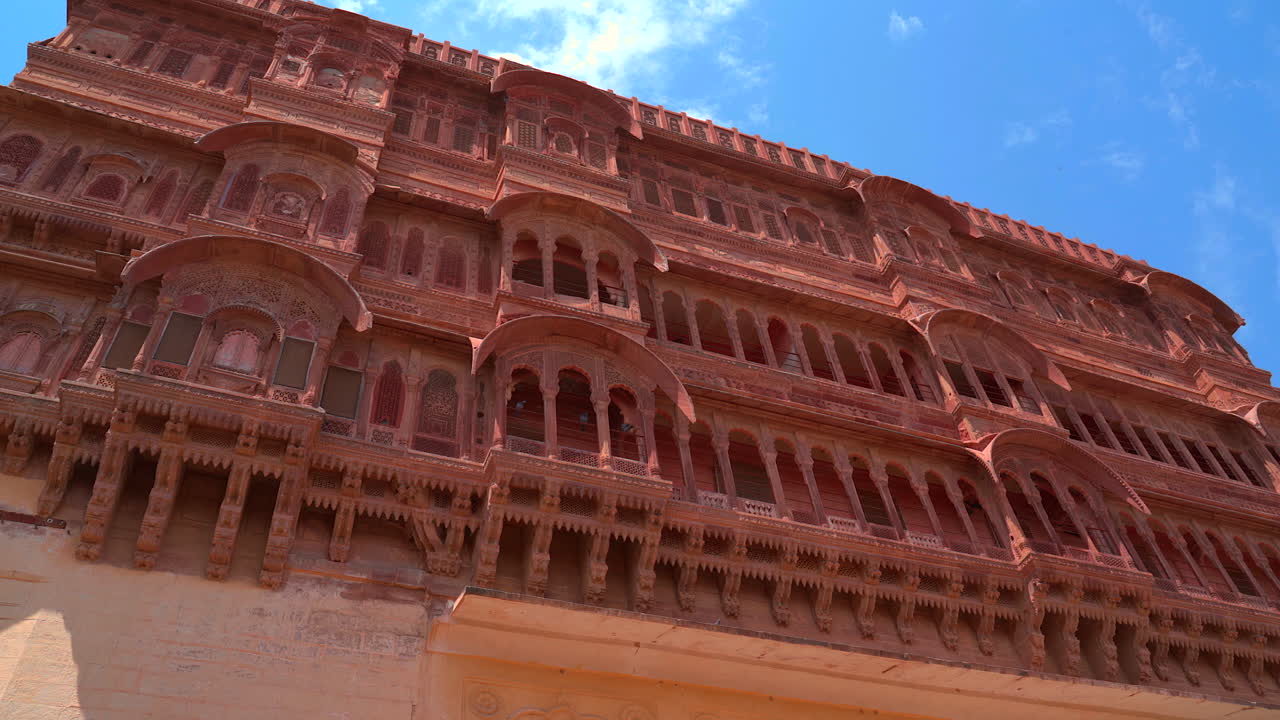 Una ripresa statica dal basso che mostra le file di balconi e finestre in arenaria rossa finemente intagliati del palazzo del Forte Mehrangarh a Jodhpur, Rajasthan, India