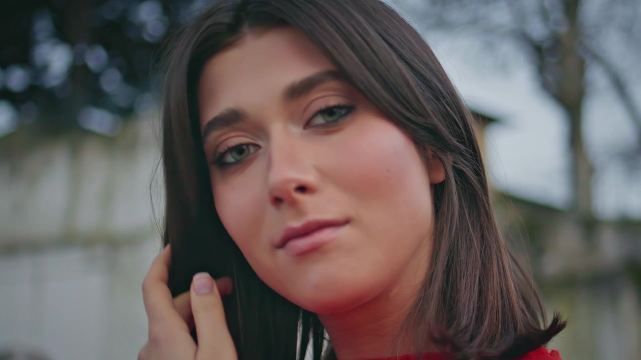 Ritratto di bella brunetta che si tocca i capelli all'aperto. Primo piano di ragazza che guarda la fotocamera.