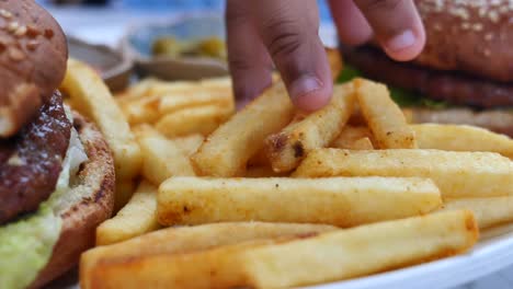 hand reaching for fries with burgers on a plate