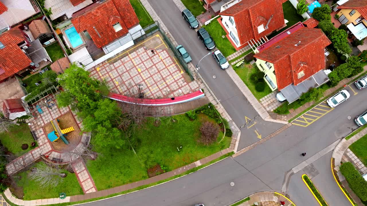 antena de arriba hacia abajo de un hombre jugando baloncesto en su patio, rodeado de casas de clase media con tejas rojas, quilpue, chile.