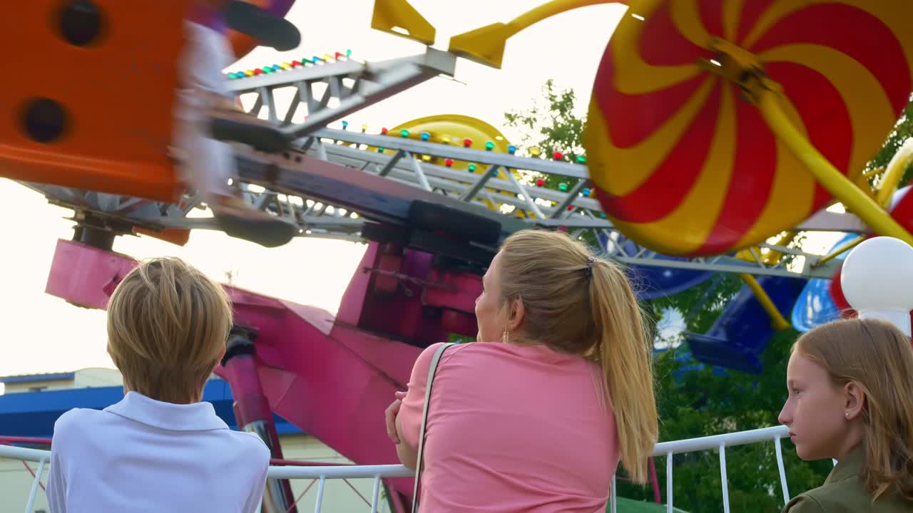 una madre con niños en un parque de atracciones, de pie junto a un carrusel que gira muy rápido, los niños están encantados con el carrusel rápido. infancia alegre en la feria del domingo