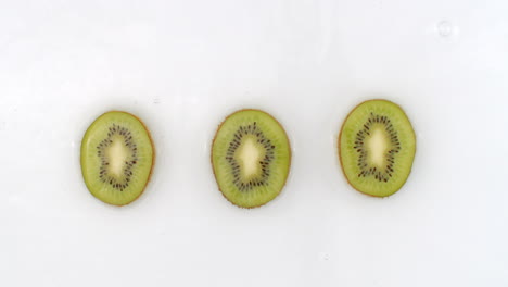 water splashes in slow motion. top view: three pieces of kiwi washed with water on a white background