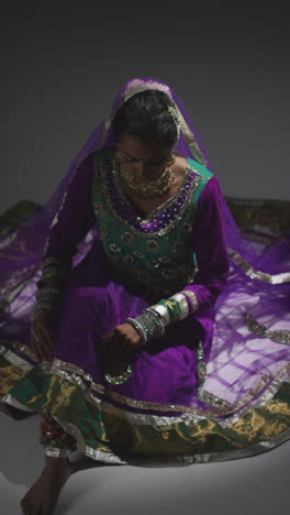 Video-Vertical-De-Una-Bailarina-De-Kathak-Arreglando-Un-Vestido-Tradicional-Indio-Antes-De-Bailar,-Sentada-En-El-Suelo-Bajo-El-Foco-De-Atención