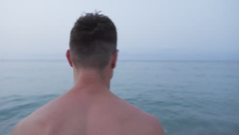 man walking into tranquil sea waters for distant swim on a grey morning