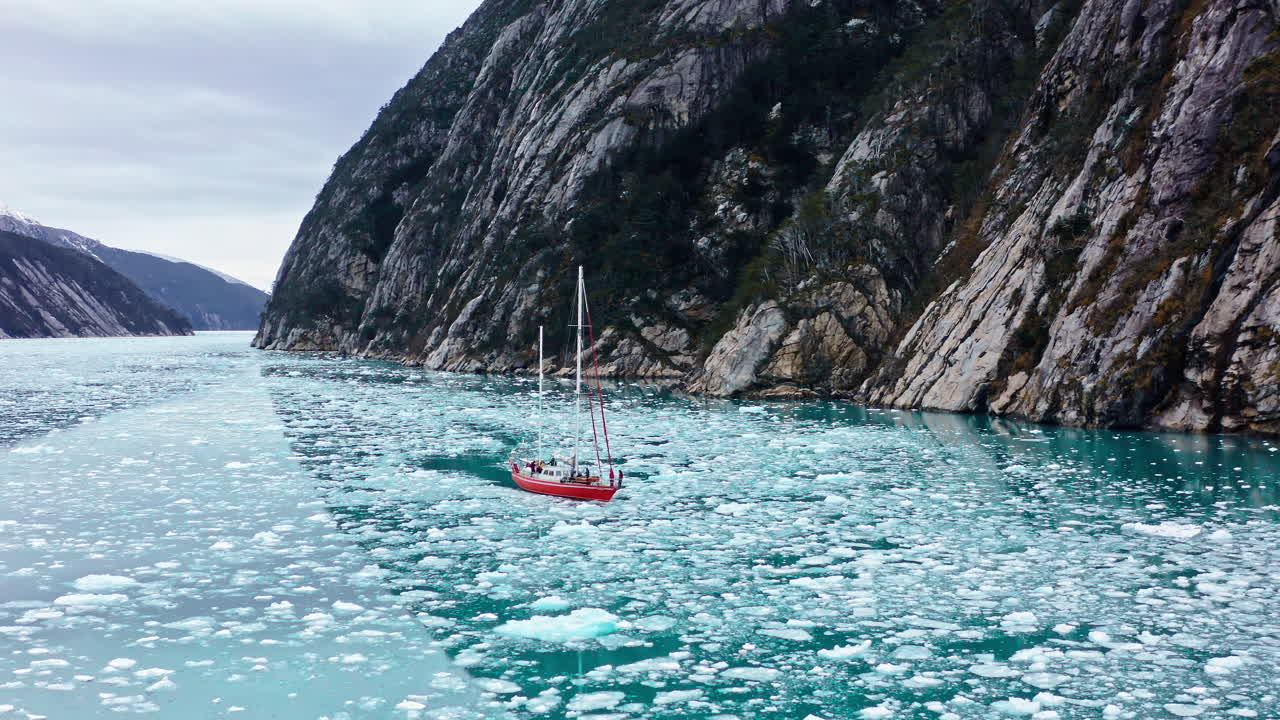Red Sailboat Navigating Through Ice Floes In Beagle Channel In South America. - aerial shot