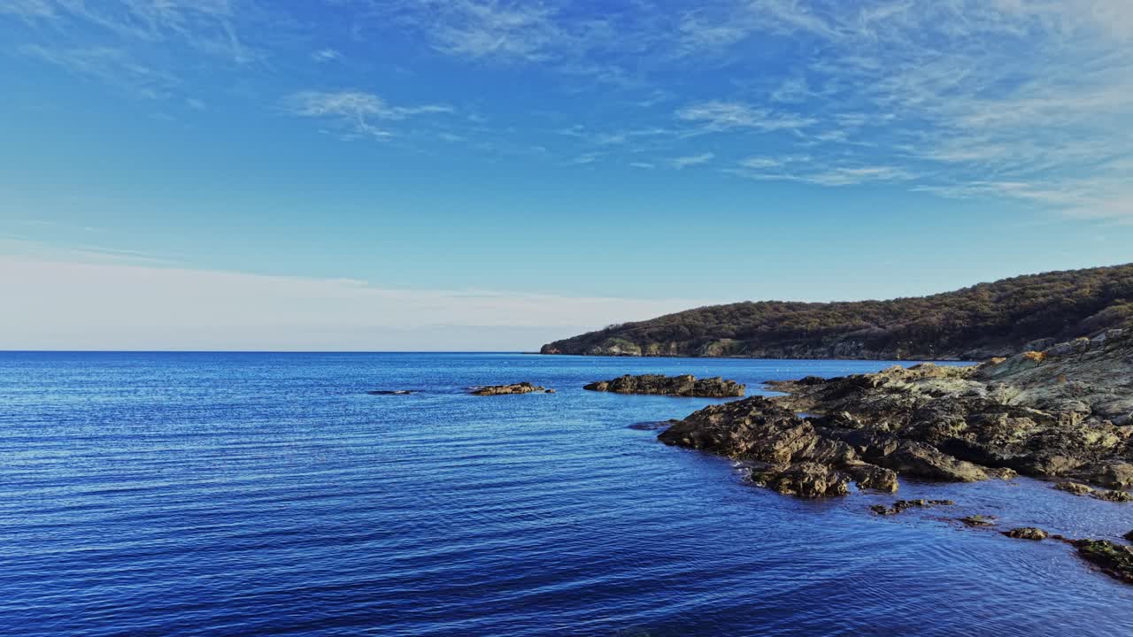 Expansive view of calm sea meeting rocky coastline under blue sky