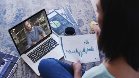 Mujer-Afroamericana-Sosteniendo-Un-Documento-Haciendo-Una-Videollamada-Con-Un-Colega-Masculino-En-Una-Computadora-Portátil