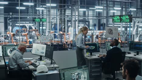 car factory: team of automotive engineers working, using computers to design advanced 3d models for high-tech engines. automated robot arm industrial assembly line manufacturing electric vehicles