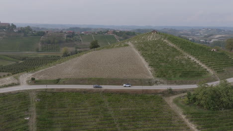 Luftaufnahmen-Einer-Silbernen-Limousine,-Die-Auf-Einer-Kleinen-Straße-Durch-Die-Weinberge-Und-Hügel-Norditaliens-Fährt