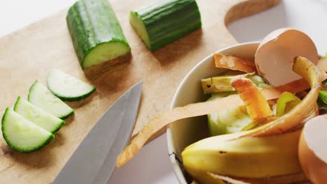 Vídeo-De-Cuchillo-Y-Pepino-Sobre-Tabla-De-Cortar,-Con-Residuos-Orgánicos-En-El-Contenedor-De-Compostaje-De-La-Cocina