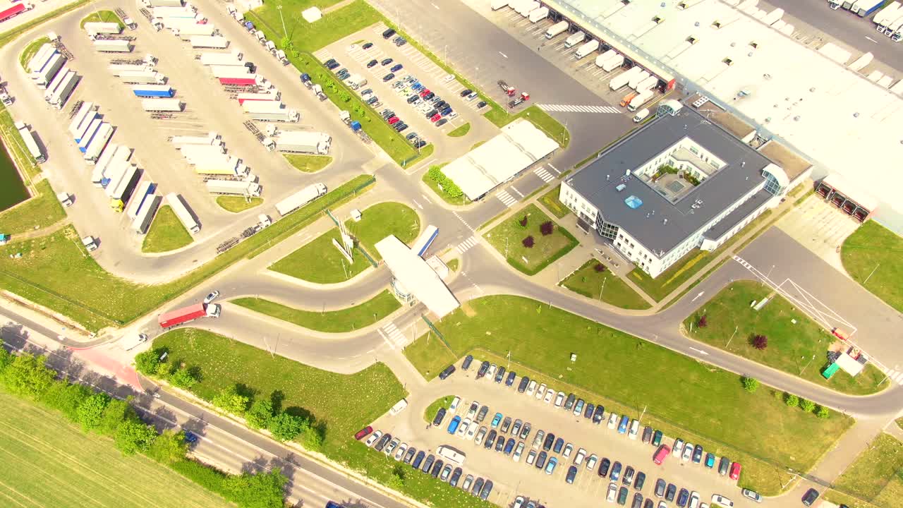 Trucks with semi-trailers stand on the parking lot of the logistics park with loading hub and wait for load and unload goods at warehouse ramps at sunset