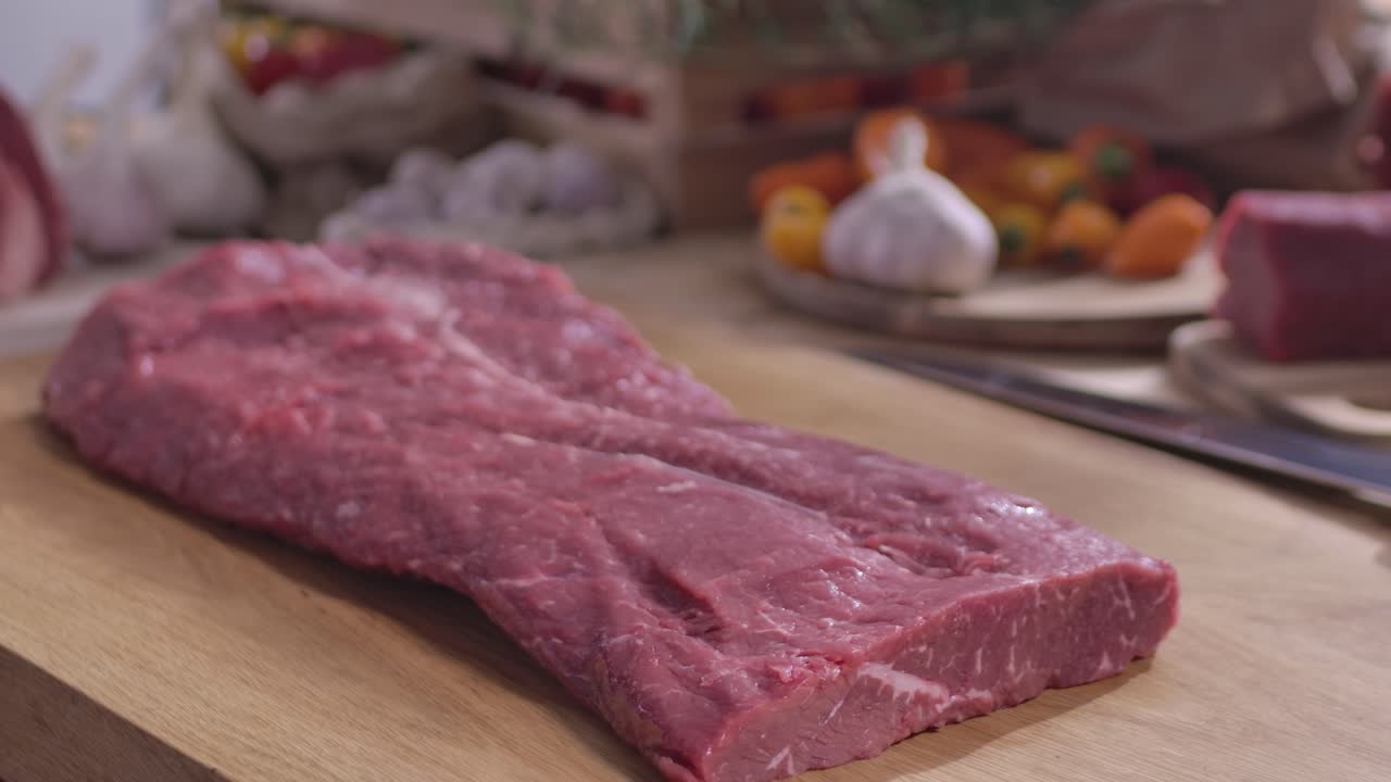 Primo piano di un macellaio che indossa guanti protettivi in nitrile nero mentre posiziona un grande taglio di carne magra cruda su un tagliere di legno per la preparazione igienica degli alimenti