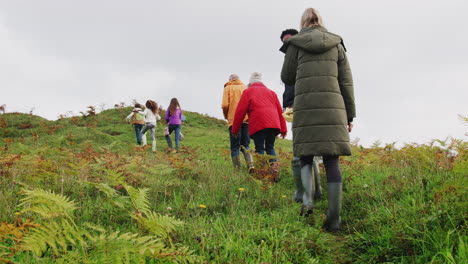 rear view of active multi-generation family on autumn walk through countryside climbing hill