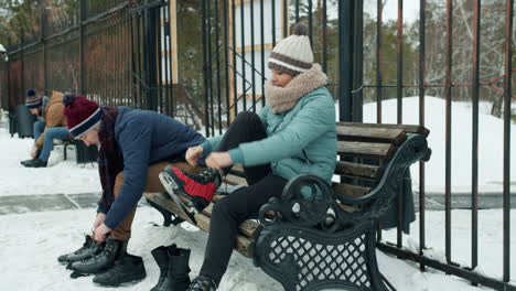 people tying ice skates in a winter park