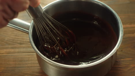 human hand stirring thick chocolate with whisk in metal pan. mixing filling