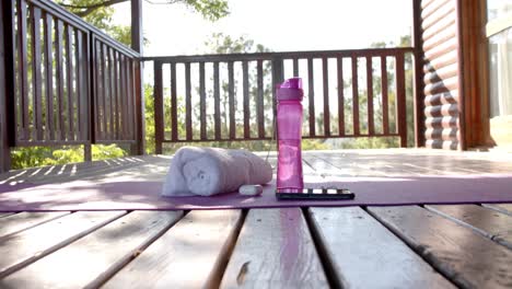 toalla, botella de agua, auriculares y teléfono inteligente en la alfombra de yoga en la cabaña de madera, cámara lenta