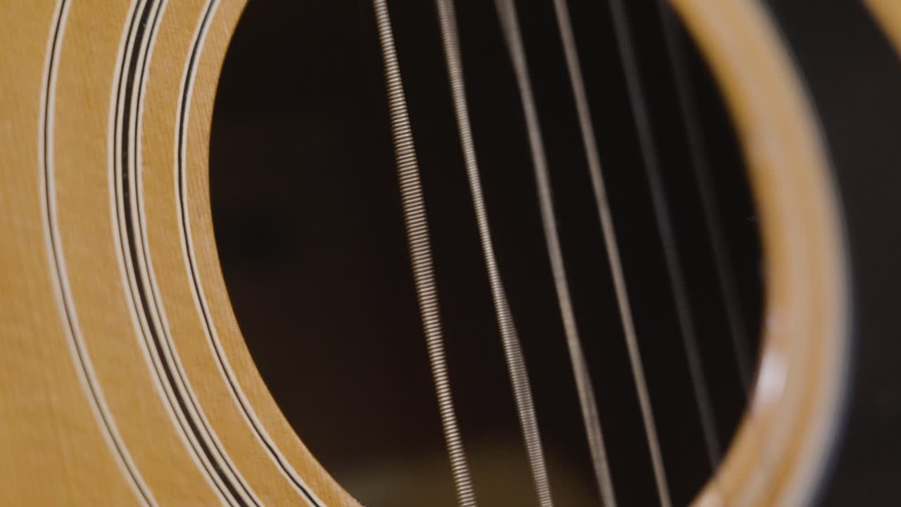 Plucking the string of an acoustic guitar in slow motion over the Sound hole