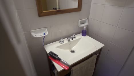 Slow right motion camera clip inside white tiled restroom in cozy house, with large sink, mirror and some hair combs on top. Shot on 4K.