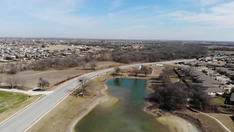 tire hacia atrás de un dron que se eleva sobre un estanque del vecindario durante el invierno con un cielo azul brillante y un camión negro que pasa