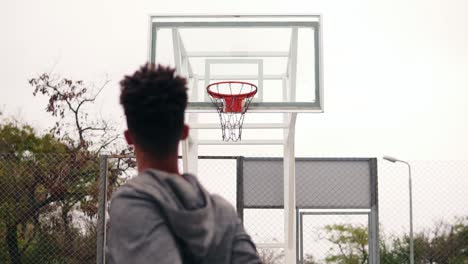 back view of unrecognizable african player throwing ball in a basketball hoop, the ball hits the ring and scores. slow motion