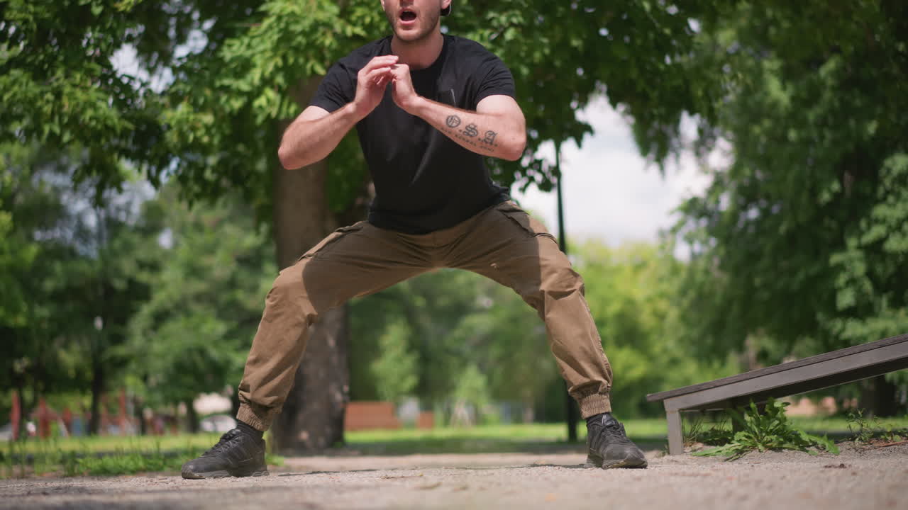 Uomo che si allena all'aperto, uomo che si allunga al mattino, uomo che esegue squat profondi all'aperto con energia focalizzata, individuo in abbigliamento casual che pratica esercizi di mobilità nel parco durante le ore mattutine