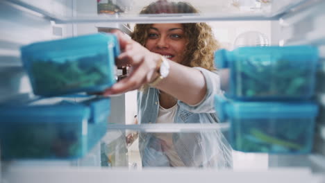 Vista-Desde-El-Interior-Del-Refrigerador-Mientras-Una-Mujer-Saca-Un-Almuerzo-Saludable-En-Un-Contenedor