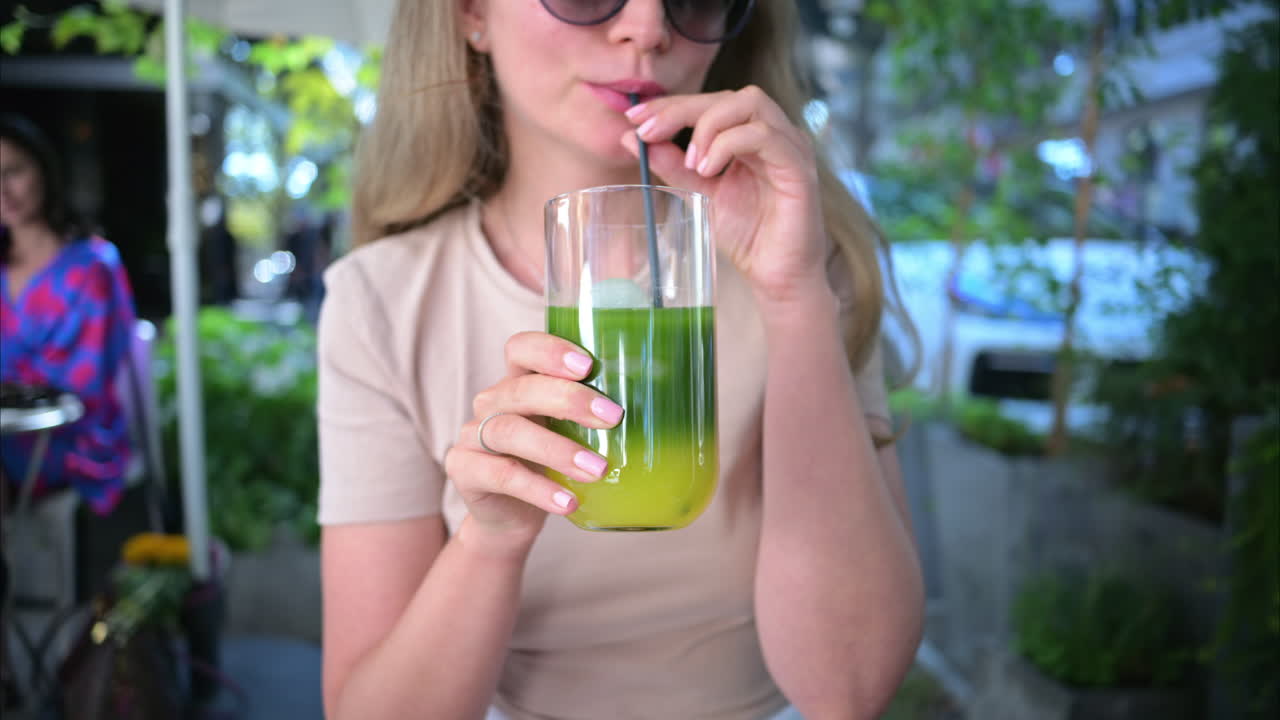 Woman drinking matcha tea with ice at a terrace, slow motion