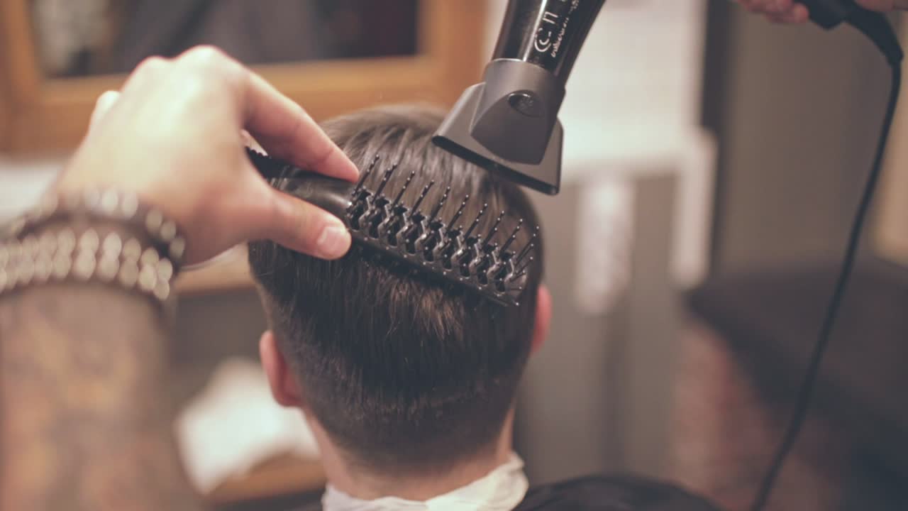 Mandlig frisure. Mand med føntørrer i barbersalon. Mandsfrisure. Mand får føntørret hår.